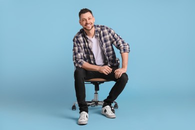 Handsome man sitting in office chair on light blue background