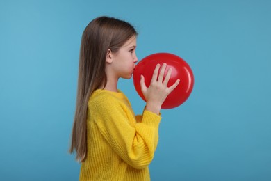 Photo of Cute girl inflating red balloon on light blue background