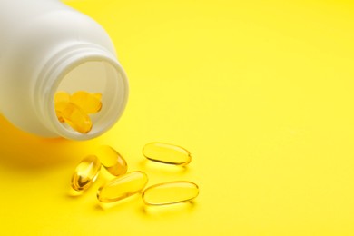 Photo of Softgel capsules and bottle on yellow background, closeup. Space for text