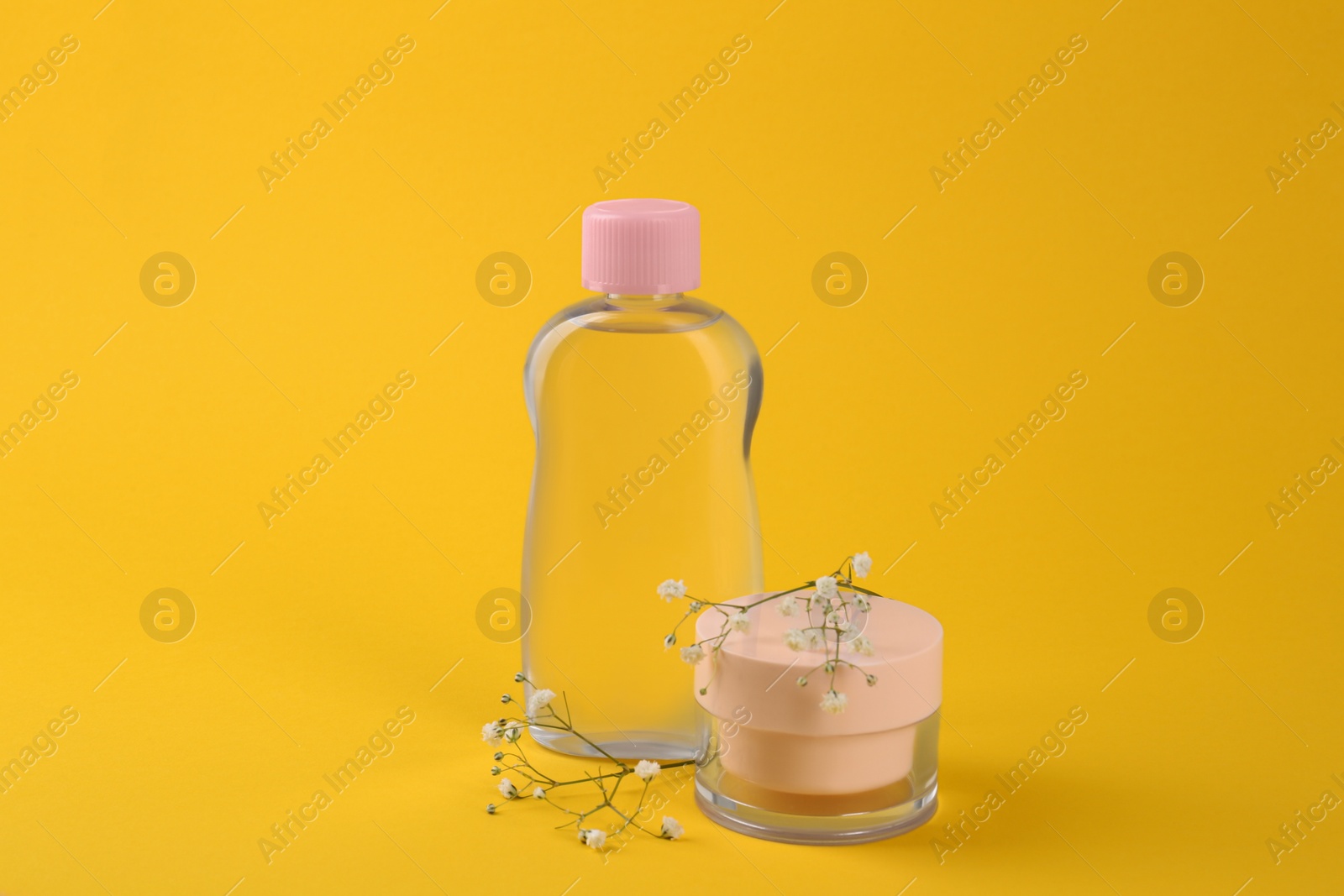 Photo of Bottle with baby oil, cream and gypsophila on yellow background