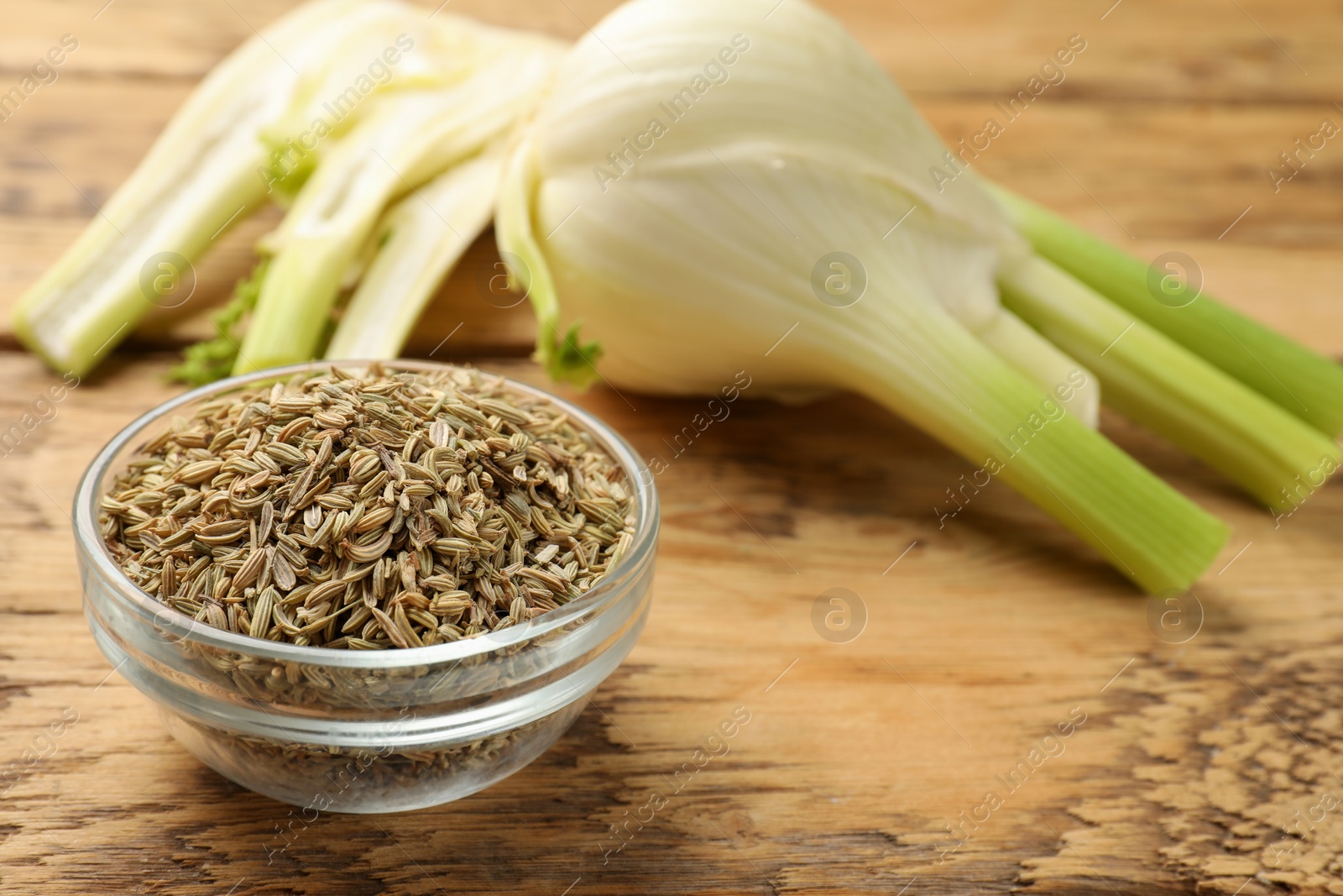 Photo of Fennel seeds in bowl and fresh vegetables on wooden table, closeup