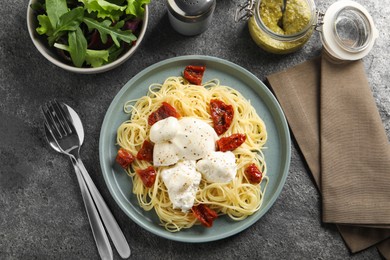 Photo of Delicious spaghetti with burrata cheese and sun dried tomatoes served on grey table, flat lay