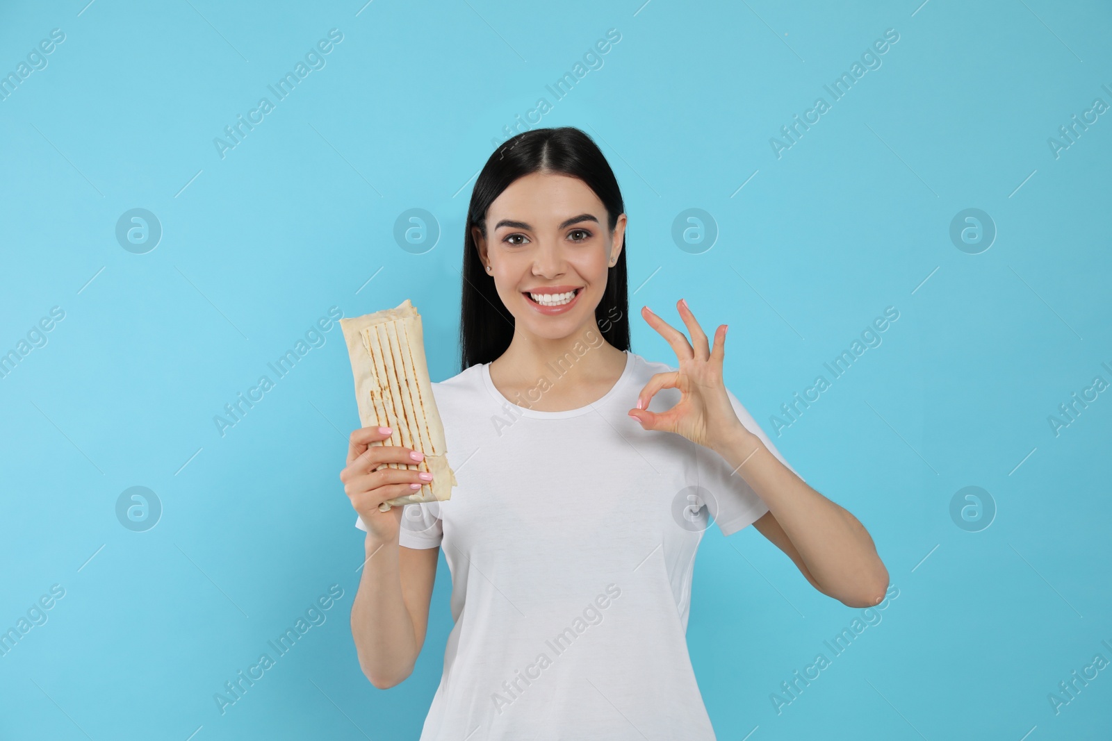 Photo of Happy young woman with delicious shawarma on light blue background