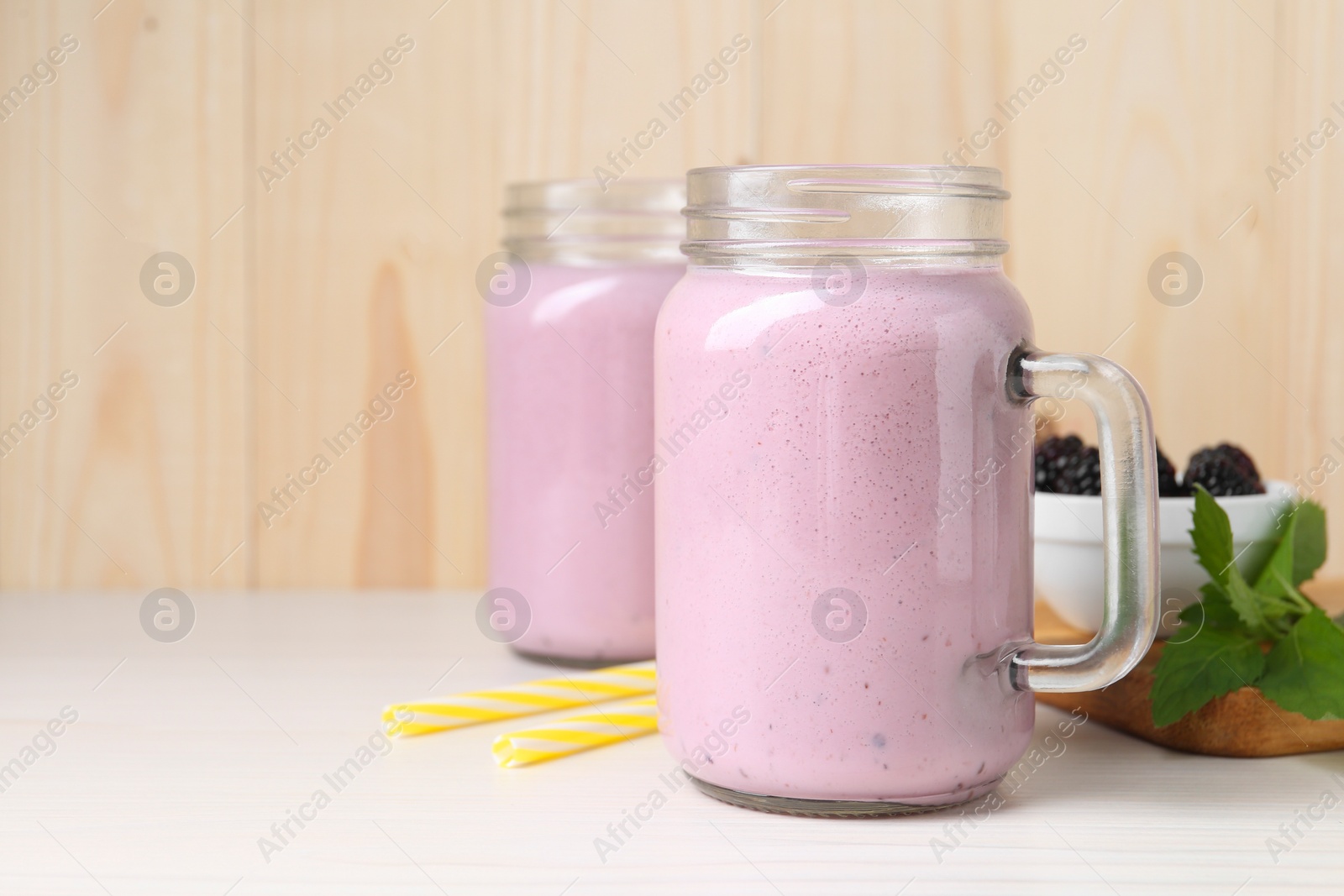 Photo of Mason jars of blackberry smoothie and mint on white wooden table. Space for text