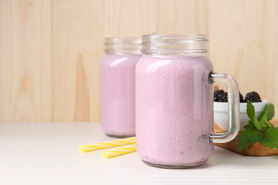 Mason jars of blackberry smoothie and mint on white wooden table. Space for text