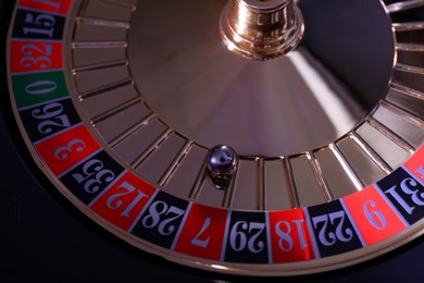 Photo of Roulette wheel with ball on dark background, top view. Casino game