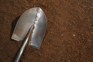 Photo of Metal shovel on fertile soil, top view and space for text. Gardening tool