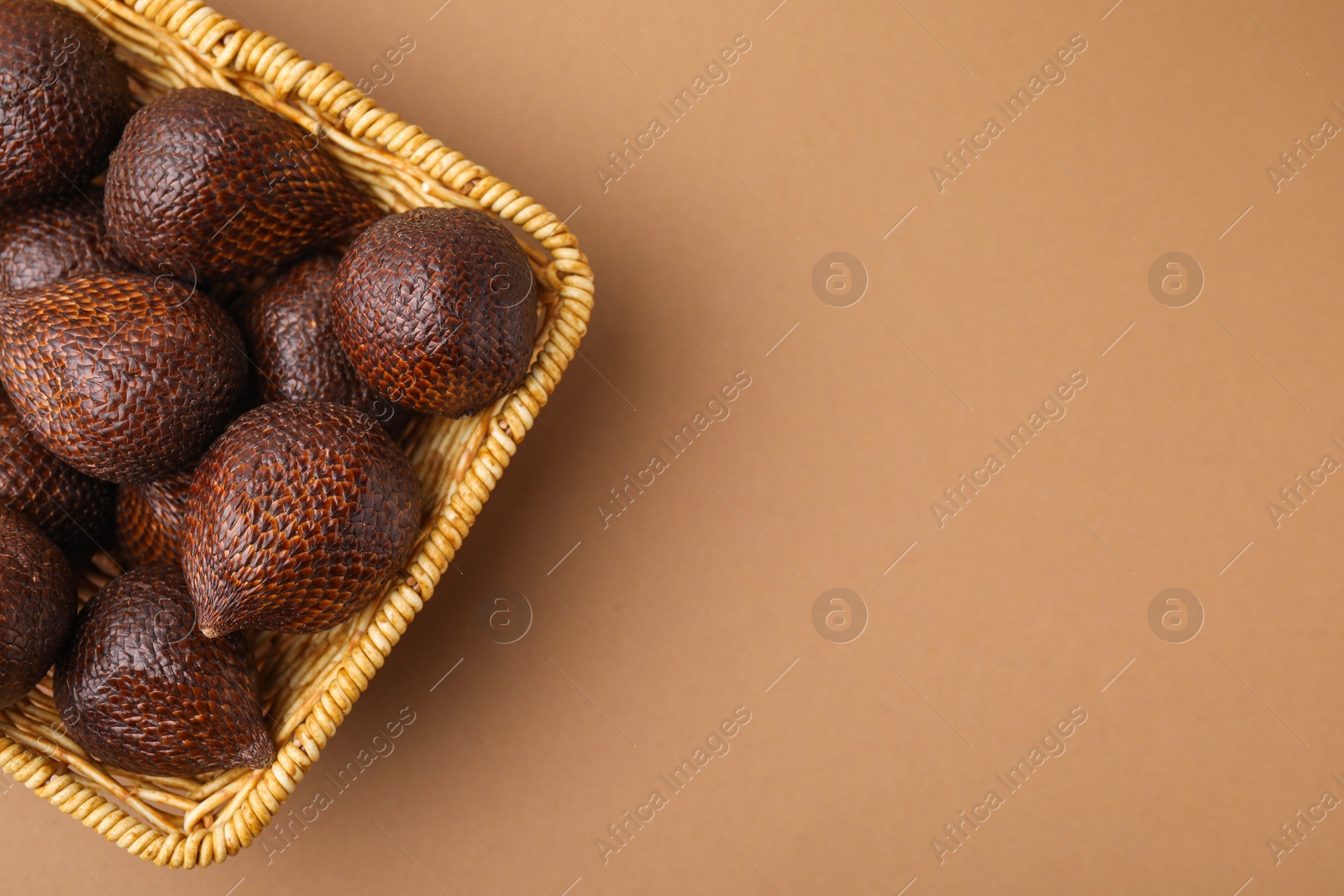 Photo of Delicious salak fruits in basket on pale brown background, top view. Space for text