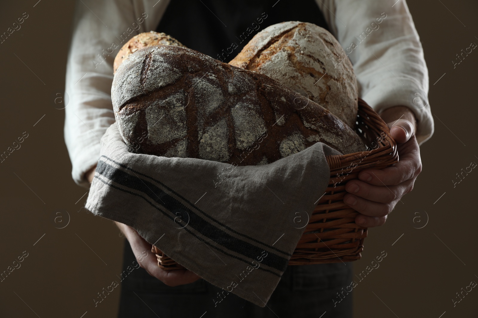 Photo of Man holding wicker basket with different types of bread on brown background, closeup