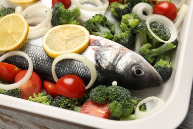 Photo of Raw fish with vegetables and lemon in baking dish on table