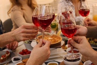 Photo of Group of people clinking glasses with red wine during brunch at table indoors, closeup