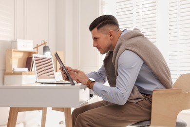 Photo of Man with poor posture using tablet at table indoors