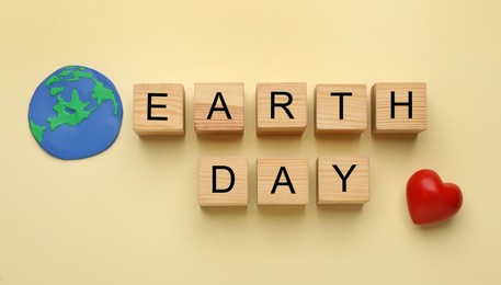 Photo of Phrase Earth Day made with wooden cubes, model of planet and red heart on beige, flat lay