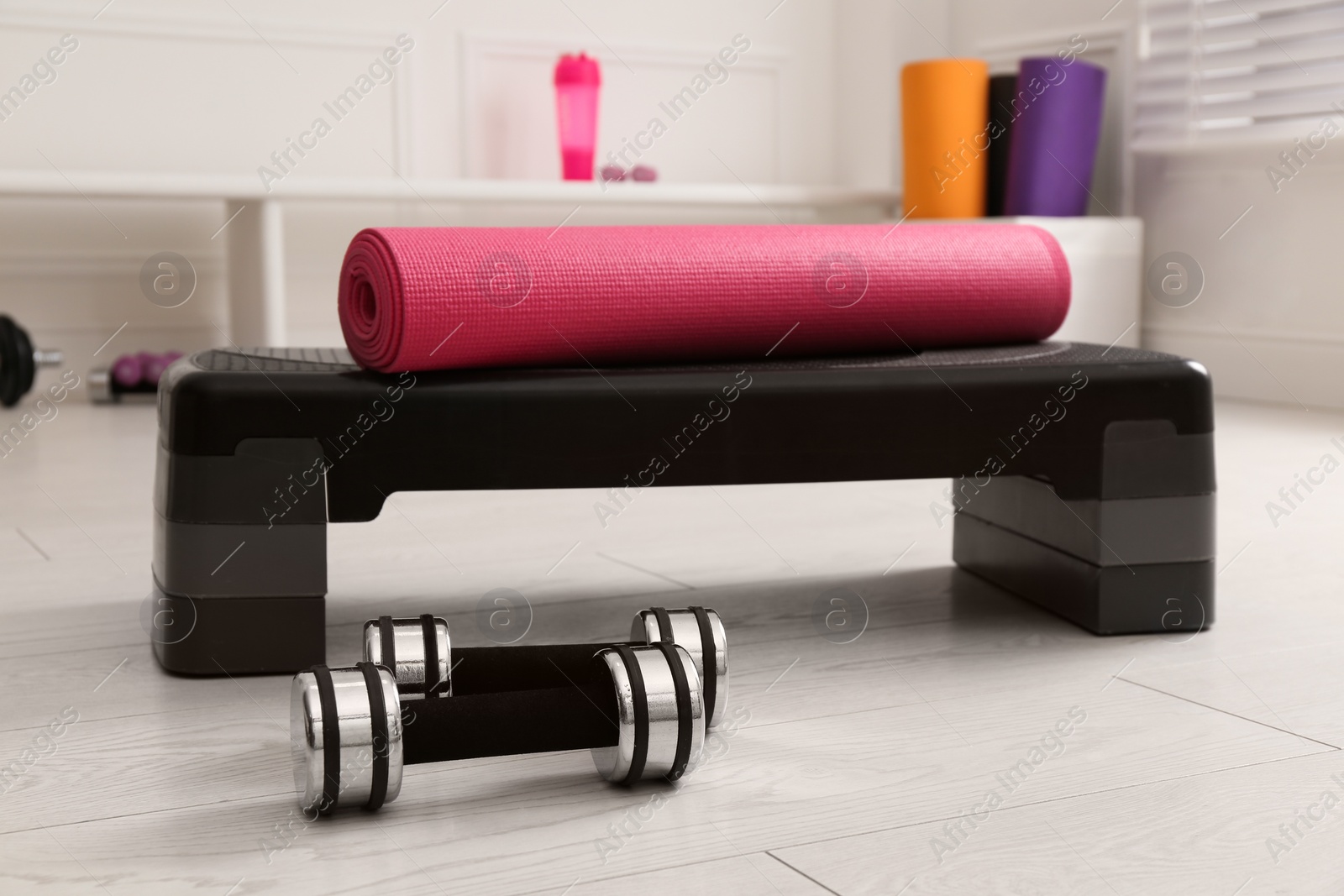 Photo of Step platform, mat and dumbbells indoors. Sports equipment