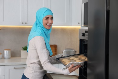 Photo of Muslim woman baking delicious cookies in oven at home