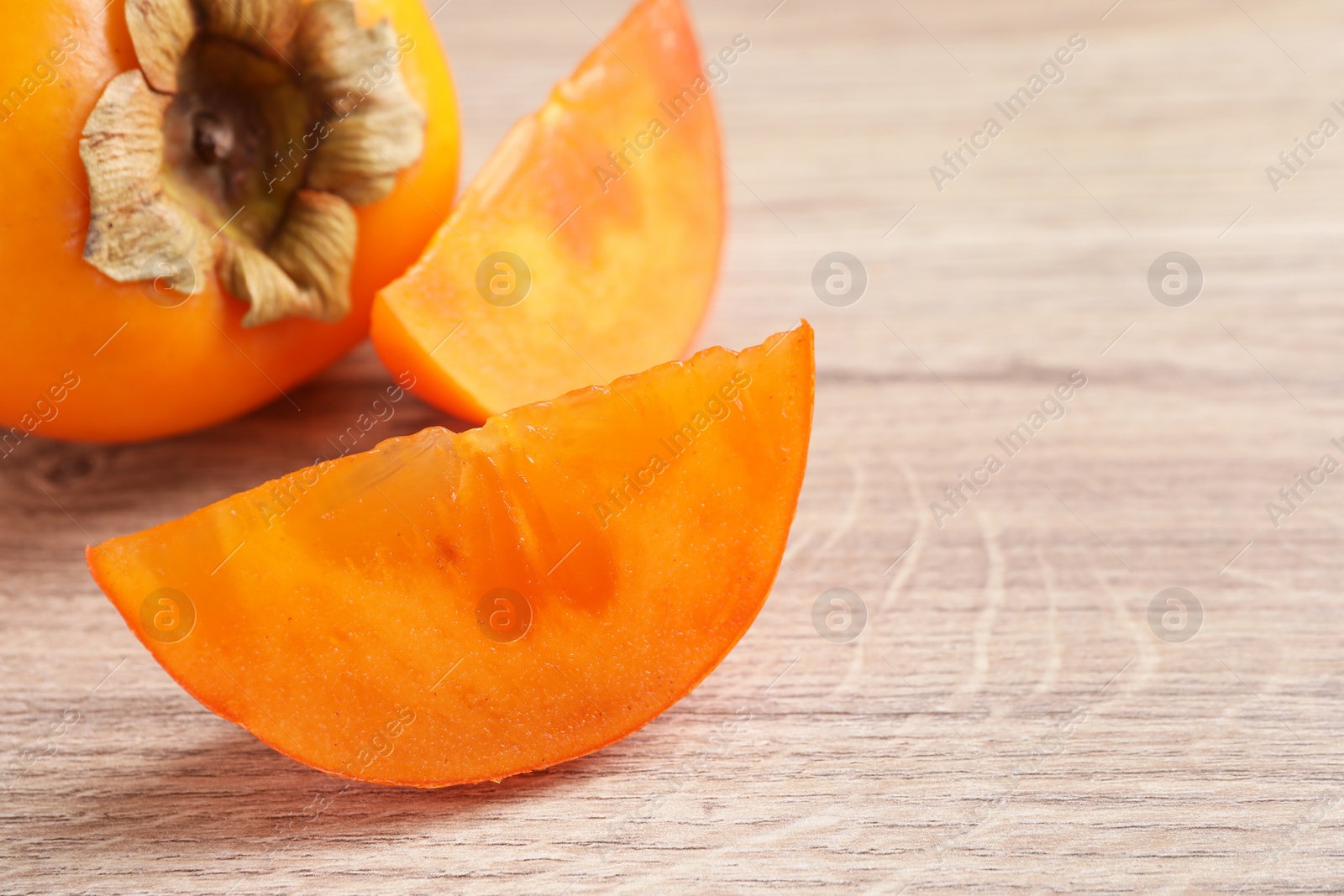 Photo of Delicious ripe persimmons on light wooden table, closeup. Space for text