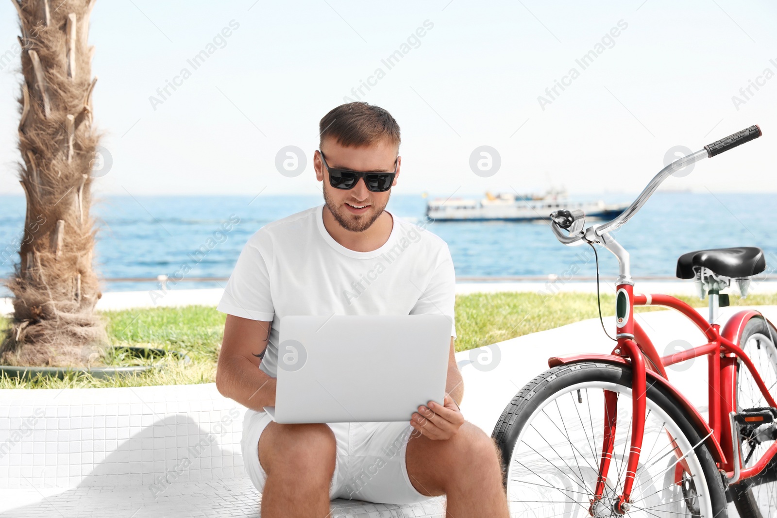 Photo of Attractive man with laptop and bike near sea