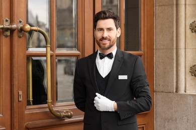 Photo of Butler in elegant suit and white gloves near wooden hotel door