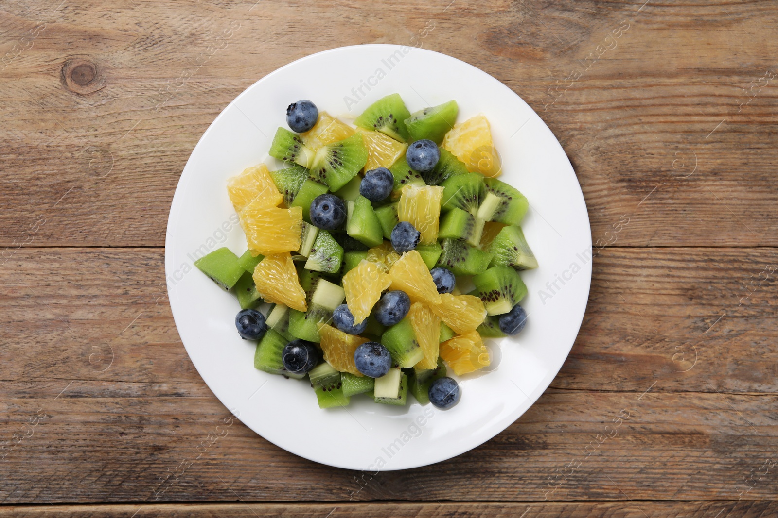 Photo of Plate of tasty fruit salad on wooden table, top view