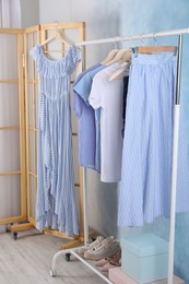 Rack with stylish clothes near light blue wall indoors