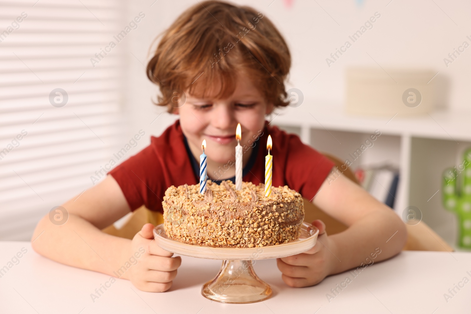 Photo of Cute boy with birthday cake at table indoors