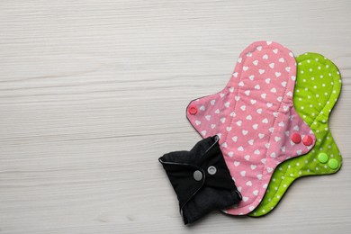 Photo of Reusable cloth menstrual pads on white wooden table, flat lay. Space for text
