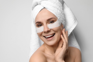 Beautiful woman with eye patches against light background. Facial mask