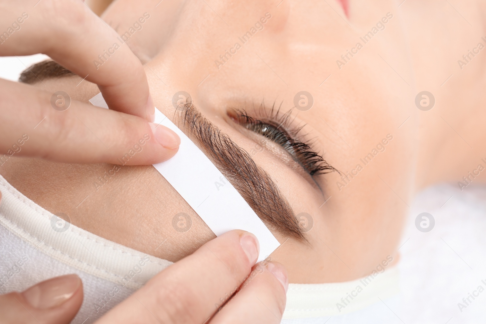 Photo of Young woman having professional eyebrow correction procedure in beauty salon