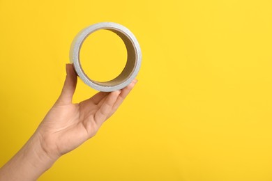 Photo of Woman holding adhesive tape on yellow background, closeup. Space for text