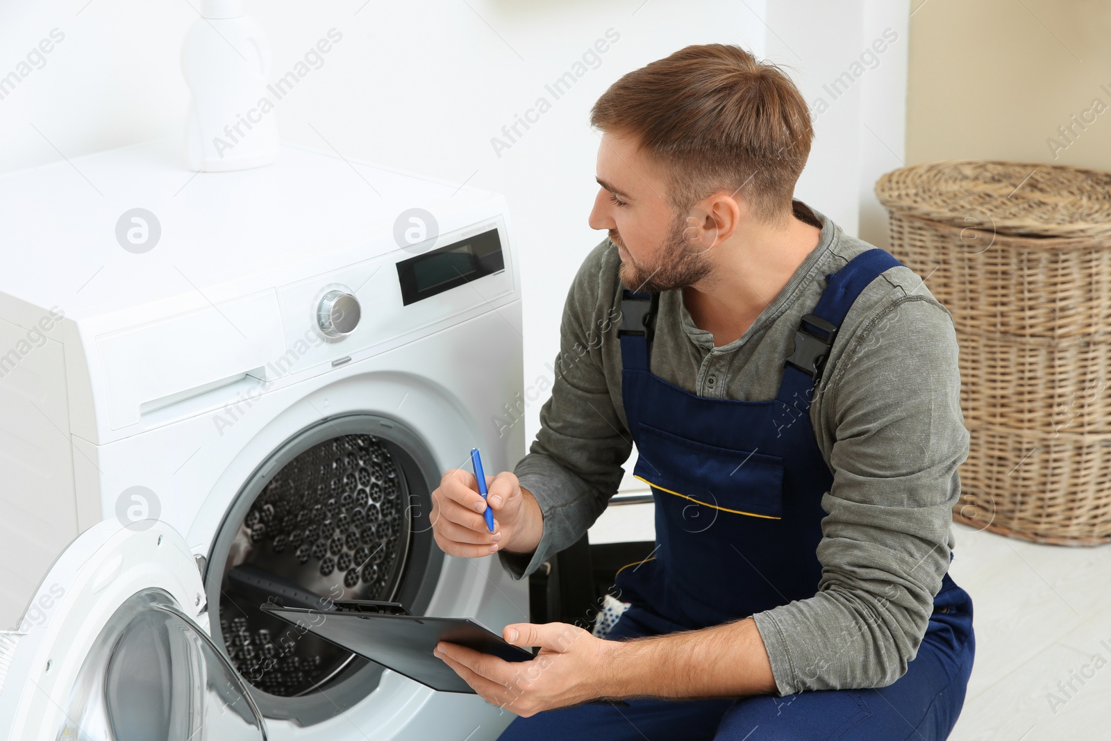 Photo of Young plumber with clipboard near washing machine in bathroom