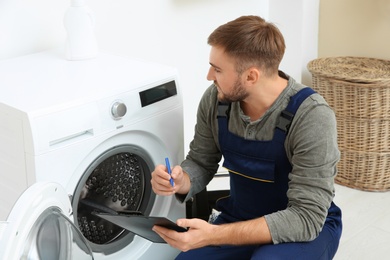 Young plumber with clipboard near washing machine in bathroom