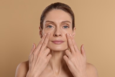 Photo of Woman massaging her face on beige background