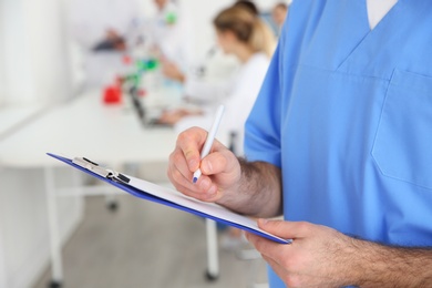 Photo of Medical student with clipboard working in scientific laboratory, closeup. Space for text