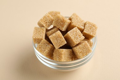 Photo of Brown sugar cubes in bowl on beige background, closeup