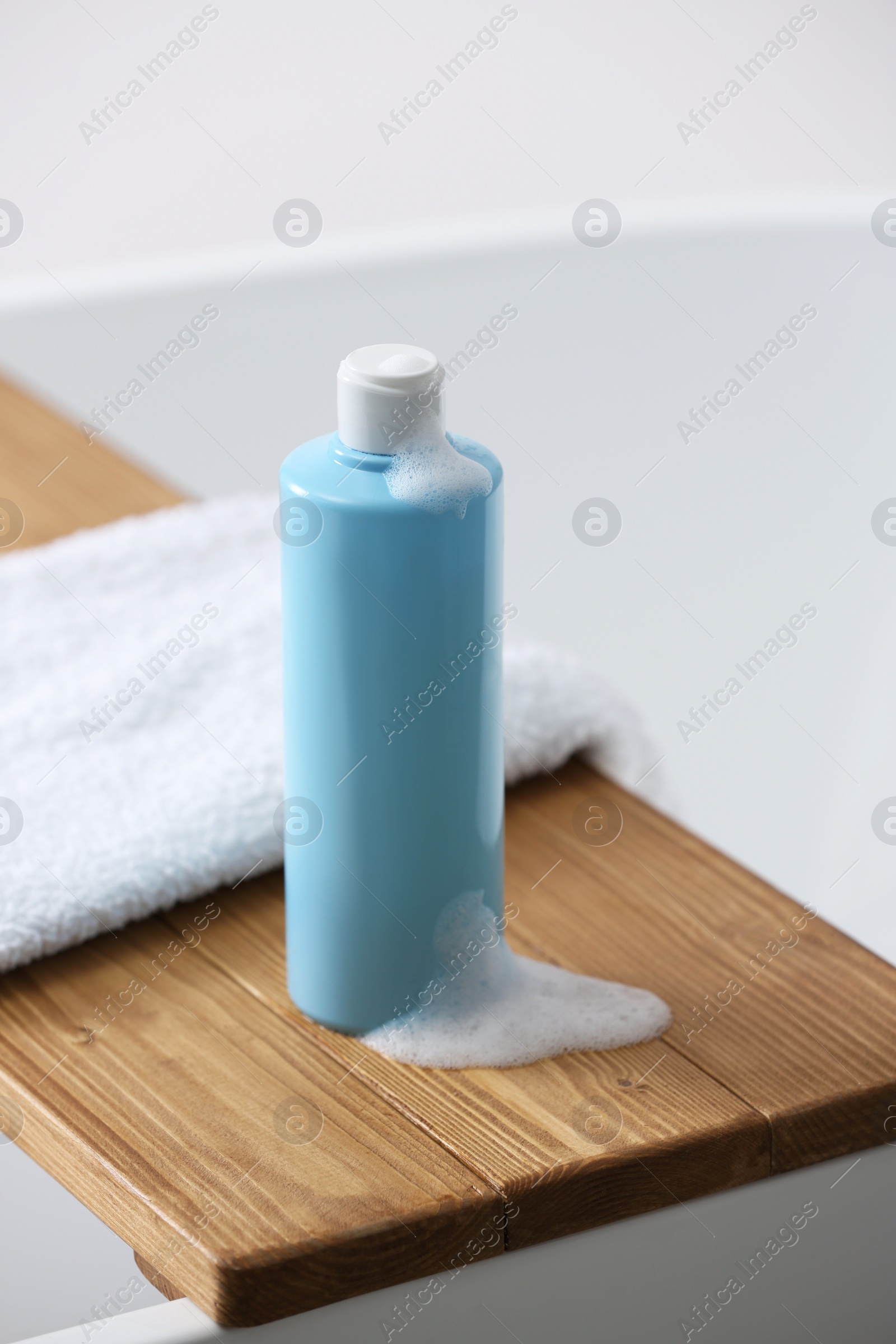 Photo of Bottle of bubble bath with foam and towel on tub in bathroom