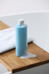 Photo of Bottle of bubble bath with foam and towel on tub in bathroom