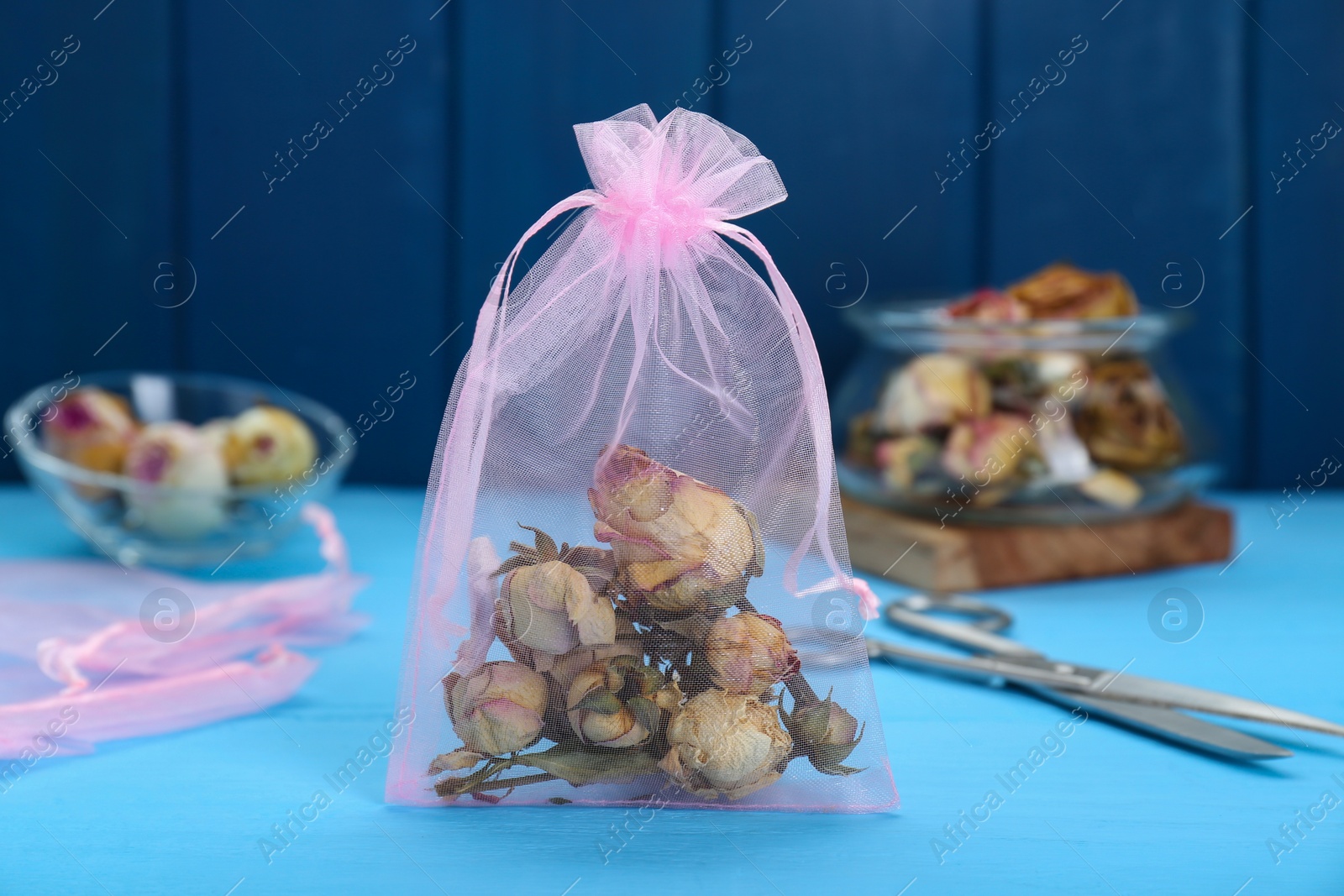 Photo of Scented sachet with dried roses on light blue table