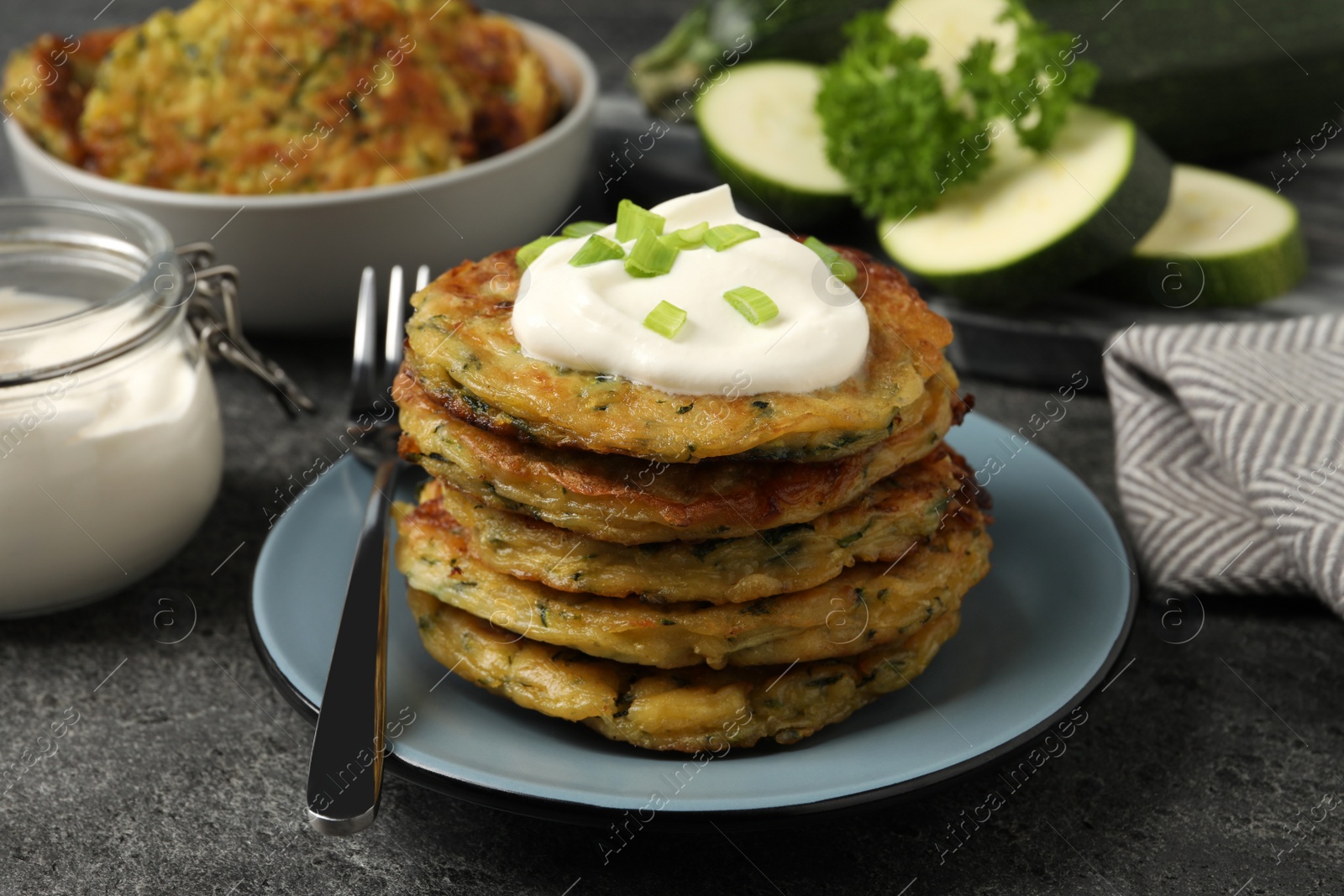 Photo of Delicious zucchini pancakes with sour cream and green onion served on grey table, closeup