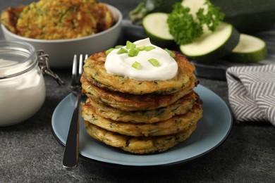 Photo of Delicious zucchini pancakes with sour cream and green onion served on grey table, closeup