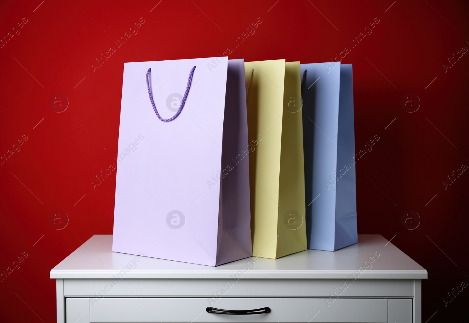 Photo of Paper shopping bags on white chest of drawers against red background