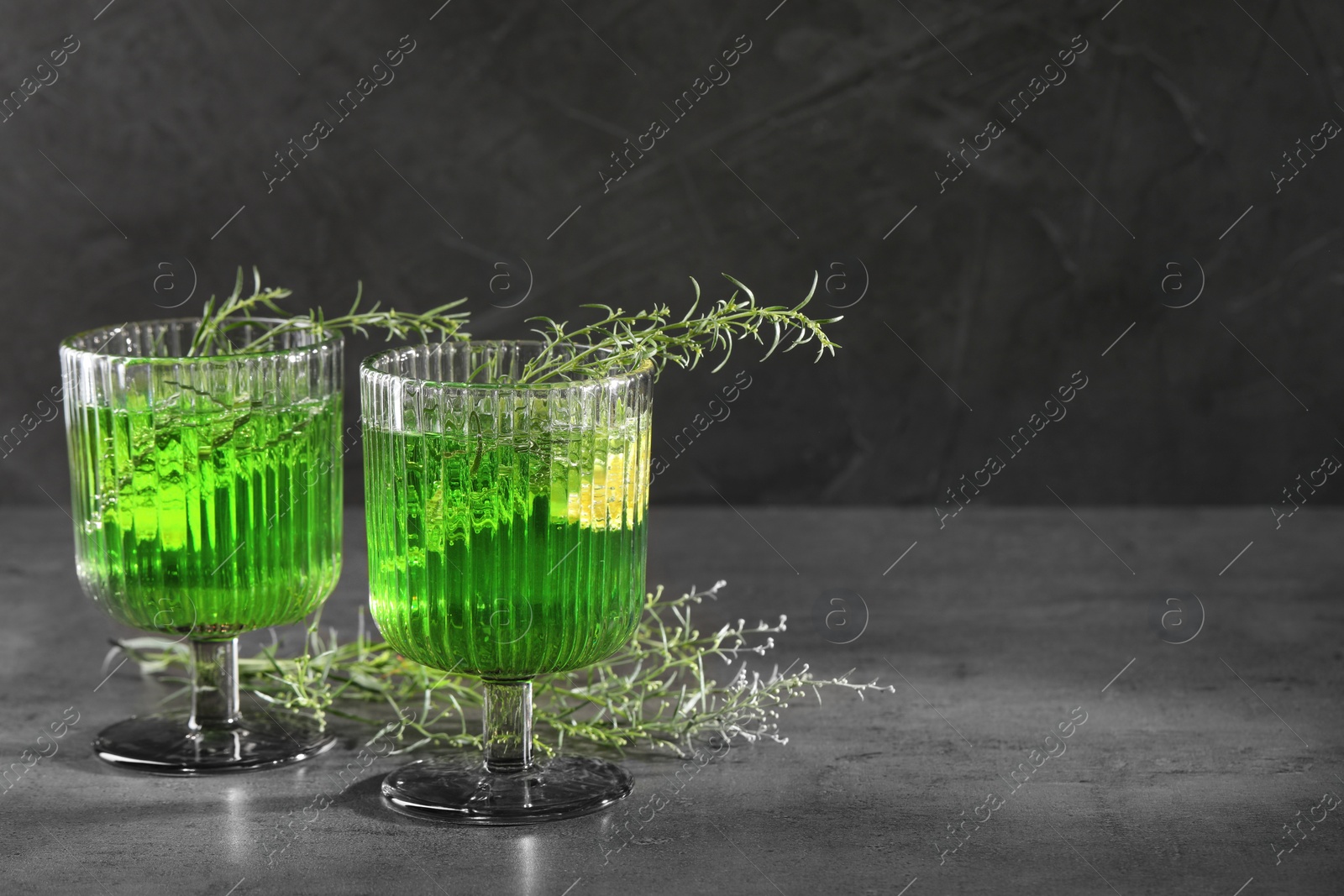 Photo of Glasses of homemade refreshing tarragon drink and sprigs on grey table, space for text