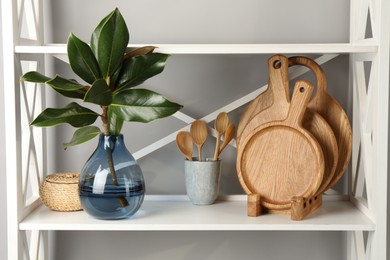 Photo of Wooden cutting boards, utensils and branch with green leaves on shelving unit