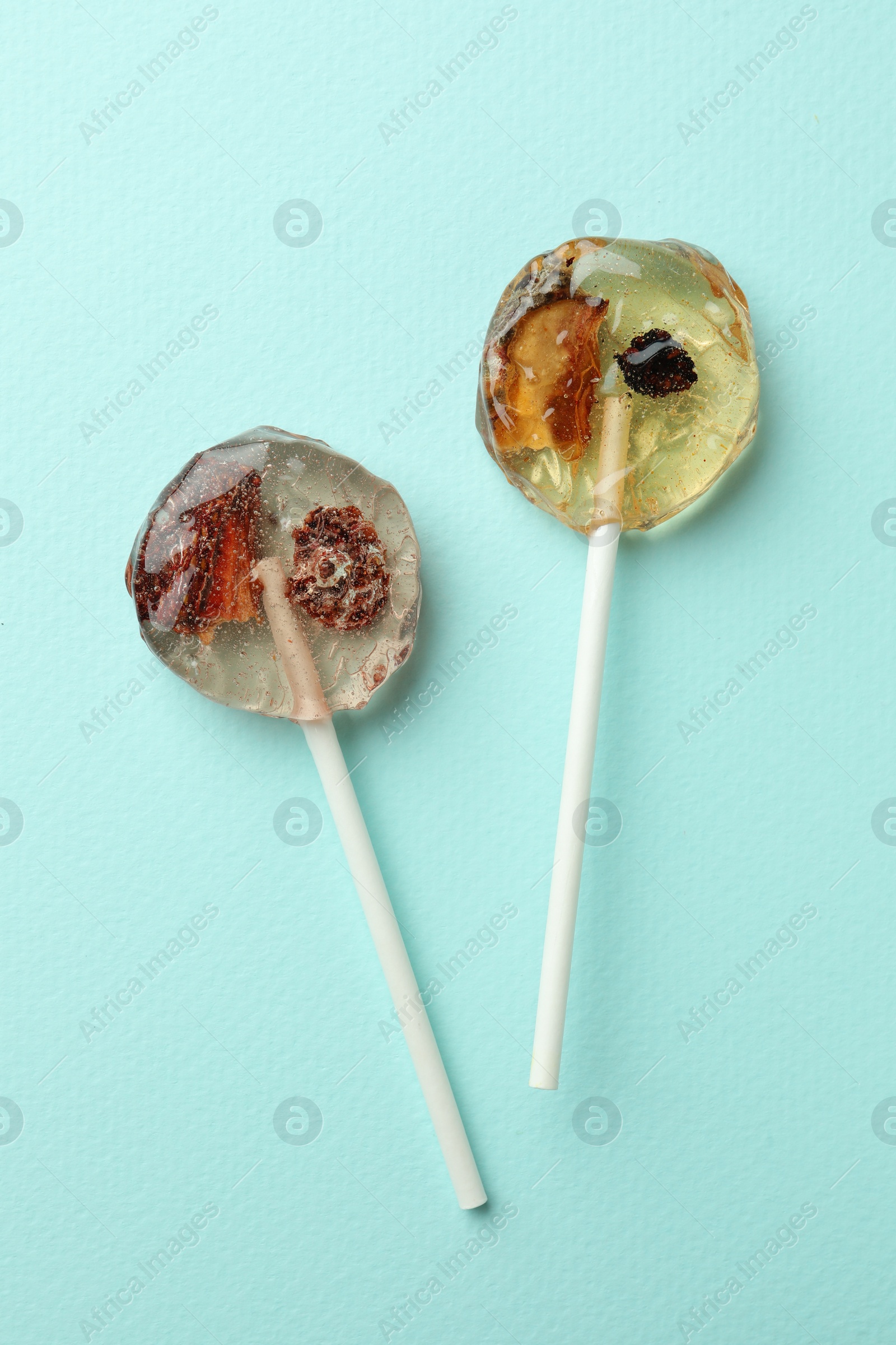 Photo of Sweet colorful lollipops with berries on turquoise background, flat lay