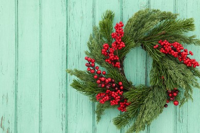 Beautiful Christmas wreath with red berries hanging on turquoise wooden wall, space for text