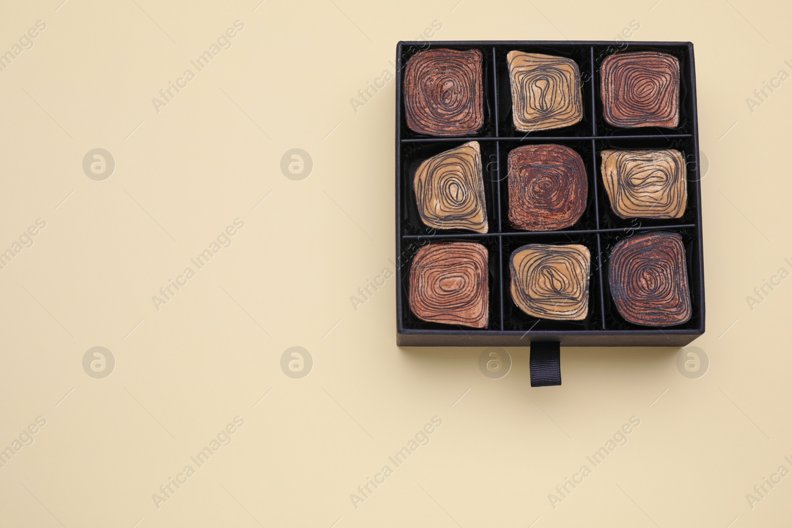 Photo of Box of tasty chocolate candies on beige background, top view. Space for text