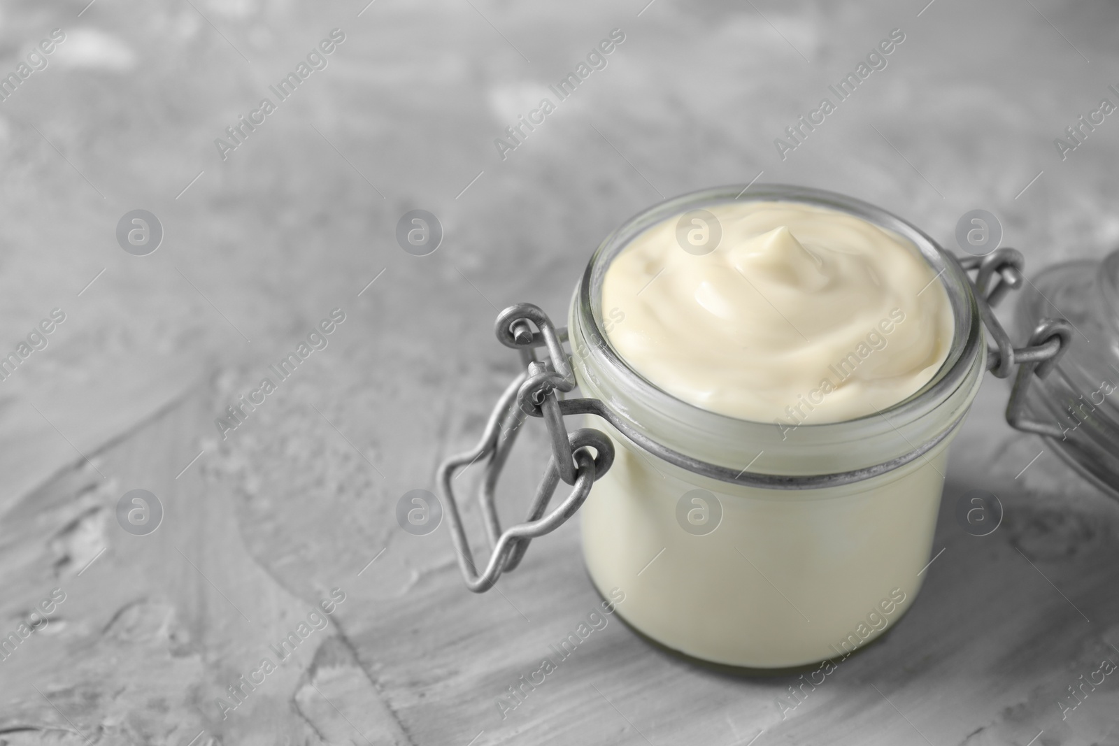 Photo of Tasty mayonnaise in jar on gray textured table, closeup. Space for text