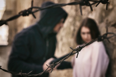 Man threatening woman with gun outdoors, view through barbed wire. Criminal offence