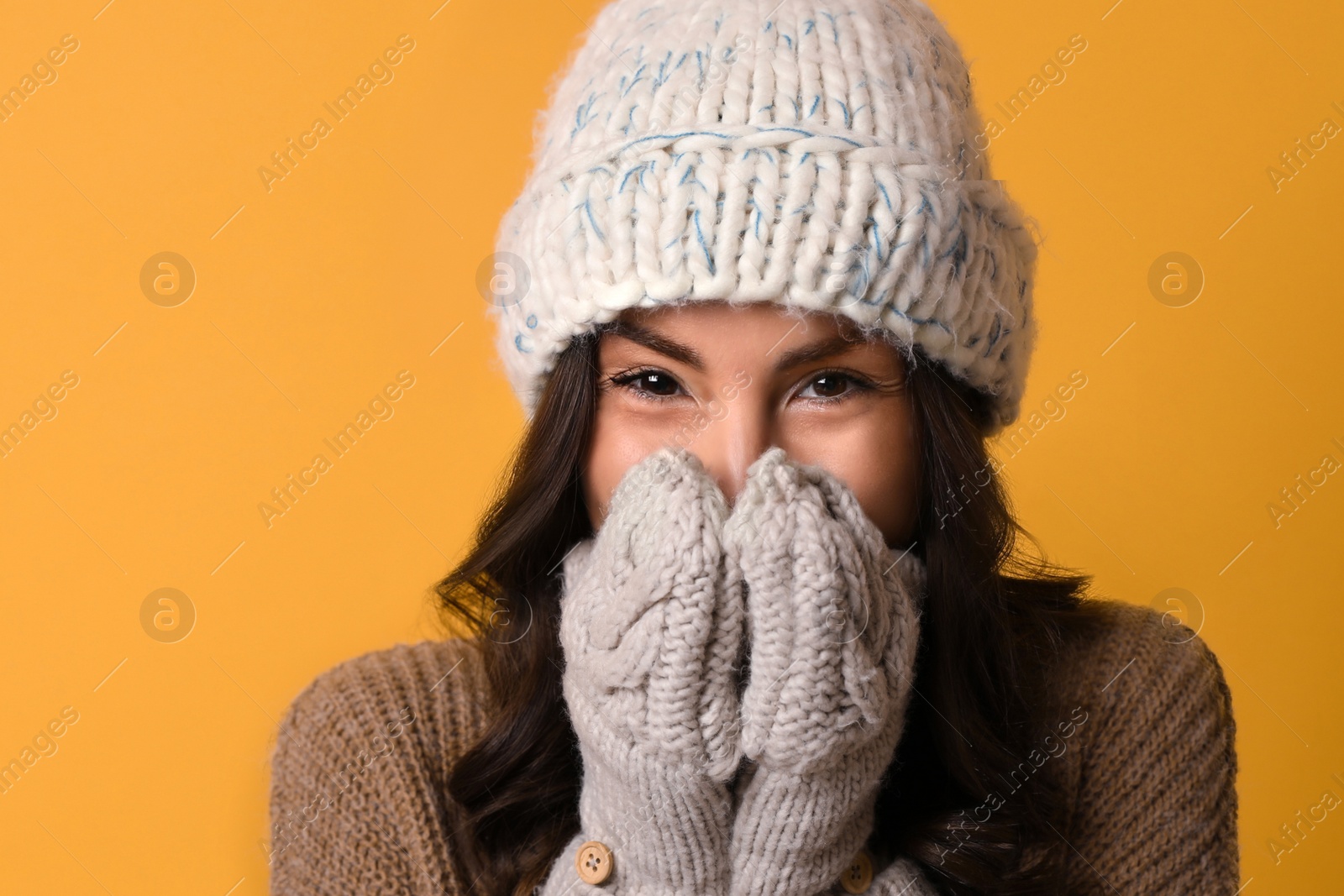 Photo of Young woman in warm sweater, hat and mittens on yellow background. Christmas season