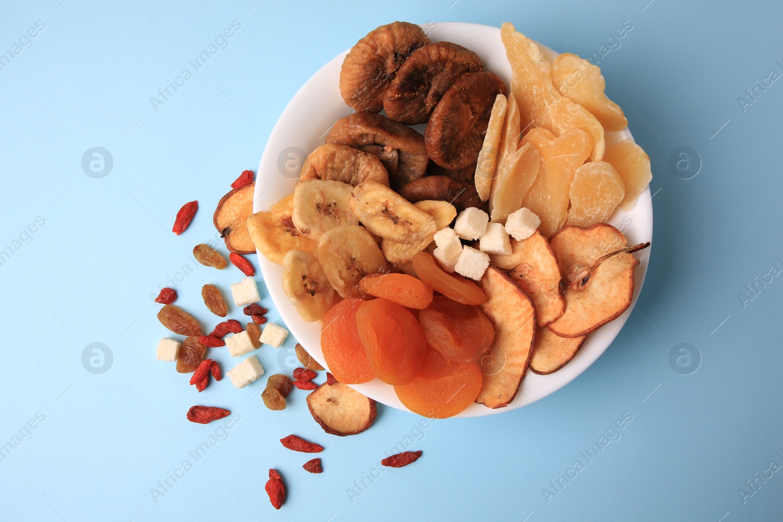 Photo of Bowl with different dried fruits on light blue background, flat lay