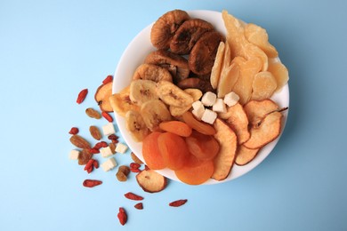 Bowl with different dried fruits on light blue background, flat lay